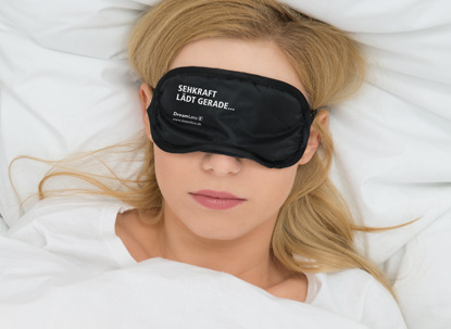 dreamLens sehkraft laedt Eine Frau trägt eine Schlafmaske mit der Aufschrift "Sehkraft lädt gerade".